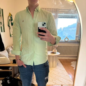 Ljusgrön skjorta från Polo Ralph Lauren - Fräsch ljusgrön skjorta från Polo Ralph Lauren i slim fit. Klassisk krage, långa ärmar och knappar hela vägen. Broderad logga på bröstet och tillverkad i mjuk bomull. OBS, lite solblekt på krage. Perfekt för dig som gillar stilrena och snygga plagg.