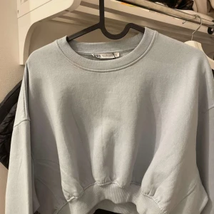 Ljusgrå croppad sweatshirt från Zara - Supersnygg ljusgrå croppad sweatshirt från Zara med rund hals och ribbade muddar. Perfekt för dig som gillar en loose fit och croppade tröjor.