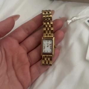 Guldig rektangulär klocka från Mockberg - Hej säljer min mockberg klocka i guld, för att jag har blivit en sliver tjej inget fel på den alls inga skador, den är köpt för 1599kr❤️ hör av er om ni vill ha fler bilder eller några frågor svara så snabbt som möjligt 