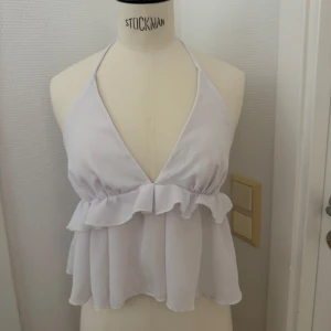 Vit volang topp med knyt i nacken - Supersöt vit topp i XS med volang och djup v-ringning. Toppen har knyt i nacken och är ärmlös med öppen rygg. Tillverkad i ett lätt och luftigt material som ger en flowy känsla. Kan hämtas på Hägerstensåsen. 🌸