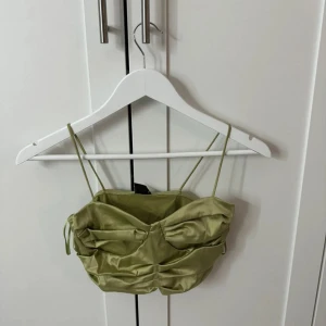 Olivgrön satin bandeau topp - Trendig olivgrön bandeau topp i glansigt satinmaterial med smala axelband och snygga rynkade detaljer framtill från gina tricot. Nypris 350