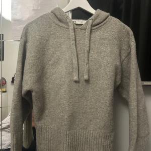 Grå stickad hoodie från Zara - Mysig grå hoodie från Zara i stickat material med huva och snörning. Tröjan har långa ärmar och bred ribbad kant vid nederdelen och ärmsluten. Perfekt nu till kyliga vintrar. nypris 599