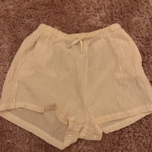 Beige/ vit shorts med snörning från H&M - Säljer ett par ljusbeige/ vit shorts från H&M med skön loose passform och elastisk midja med snörning. Materialet är lätt och krinklat, perfekt för varma dagar. De har en enkel design utan mönster och är riktigt bekväma att bära.