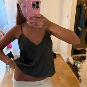 Mörk grön linnetopp med smala axelband - Säljer en mörk grön silke topp med smala axelband och v-ringad.  Perfekt att styla med kjol eller jeans för en enkel men snygg look.