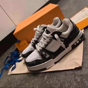 Louis Vuitton svartvita sneakers - Louis Vuitton sneakers i svart och vitt med klassiskt monogrammönster och tydlig logga på sulan. Skorna har snörning, platt sula och rund tå. Materialet är skinn och syntet, och detaljerna är riktigt cleana med kontrasterande färger och LV branding på sidan.