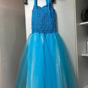 Turkos barnklänning från Minisa - Säljer en turkos barnklänning från Minisa med smockad överdel och axelband. Kjolen är gjord i flera lager tunn tyll med små pärldetaljer som ger extra glans. Ny med prislapp aldrig använd 