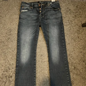 Bootcut jeans från LTB, blå W30 L32 - Snygga blå bootcut jeans från LTB med klassisk femficksdesign och kontrastsömmar. Jeansen har knäppning med flera kopparfärgade knappar och cool faded effekt framtill och baktill. Passar dig som gillar en lite bredare benslut och stilren look.