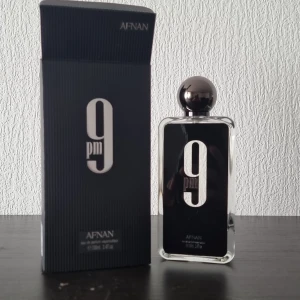 Afnan 9PM Eau de Parfum 100ml - Afnan 9PM Eau de Parfum i en stilren, rektangulär glasflaska med svart etikett och stor silverfärgad kula som lock. Kommer med matchande svart kartong med tydlig logga. Flaskan rymmer 100ml och har en modern, elegant design.