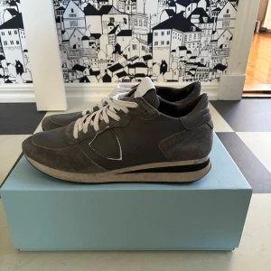 Philippe Model skor - Tjena, säljer just nu ett par snygga grå sneakers från Philippe Model i storlek 41 med vita snören och detaljer i mocka och skinn. Klassisk rund tå och platt sula, perfekt för dig som gillar stilrena och sportiga skor. Diskret logga på sidan och svart yttersula. Passar dig som vill ha en clean look, hojta om ni har några frågor😁