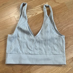 Ljusgrå ribbad linnetopp H&M - Supersnygg ljusgrå linnetopp från H&M med ribbad struktur och kabelstickat mönster. Djup v-ringning och bred resår nedtill ger en sportig och trendig look. Perfekt att styla med jeans eller kjol för en chill vibe.