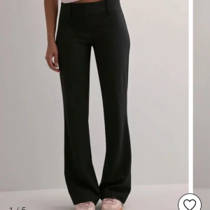 Svarta lågmidjade kostymbyxor Nelly - Säljer ett par svarta kostymbyxor från Nelly i storlek 34. Byxorna har superlåg midja, utsvängda ben och klassisk kostymlook med bälteshällor. Snygg flare och stilren passform som ger en cool siluett. Perfekta till sneakers eller klackar.