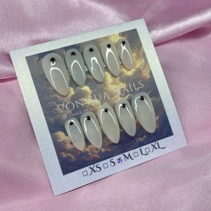 Cappu (M);Medium Almond - Snygga handgjorda press-on naglar i en cool vit nyans med svart prickdetalj vid nagelroten. Naglarna har en medium almondform och en glansig finish. Perfekt för dig som vill ha en stilren och edgy look. Finns i M: 16 mm, 12 mm, 12,5 mm, 11,5 mm, 10 mm 