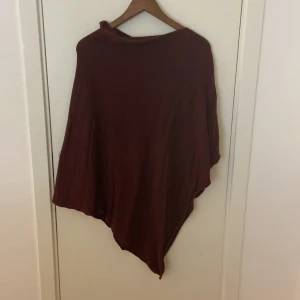 Vinröd poncho polotröja - Säljer en vinröd polotröja med ponchoformad siluett. Tröjan har en lös passning och är tillverkad i mjukt material som faller snyggt. Perfekt för dig som gillar chill och oversized vibe. Passar till lager-på-lager och har en enkel, stilren look.