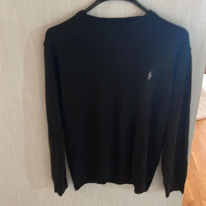 Svart tröja från Polo Ralph Lauren - Svart långärmad tröja från Polo Ralph Lauren i storlek M. Klassisk design med rund hals och den ikoniska broderade loggan på bröstet. Perfekt för dig som gillar stilrena och tidlösa plagg. Materialet känns mjukt och skönt mot huden.