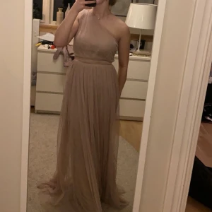 Ljusrosa långklänning med oneshoulder - Säljer nu min fina balklänning som är en elegant ljusrosa långklänning med oneshoulder och markerad midja. Klänningen har ett svepande, plisserat tyg som ger ett romantiskt och luftigt intryck. Perfekt för bal eller student. Passformen är normal och klänningen är oneshoulder med en axelbandslös design. Endast använd en kväll. 