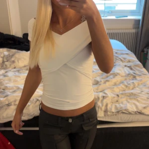 Vit omlott offshoulder topp - Snygg vit omlott topp med offshoulder-design och croppad passform. Tunn och mjuk, perfekt för dig som gillar stilrena och trendiga plagg. Sitter tight och framhäver axlarna på ett coolt sätt. Enkel att matcha med både jeans och kjol.