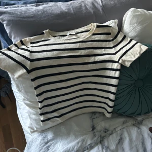 Randig vit och svart topp - Snygg vit topp med svarta horisontella ränder och rund hals. Modellen är kortärmad och har en klassisk, lite loose passform. Perfekt för dig som gillar enkel och stilren design med en touch av Paris-vibe.