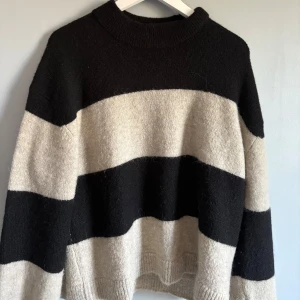 Randig stickad tröja i svart och beige - Säljer en oversized stickad tröja med breda svarta och beige ränder. Tröjan har rund hals, långa ärmar och mjuk, mysig känsla. 
