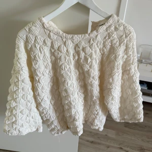 Vit blus från Carin Wester med struktur - Säljer en vit blus från Carin Wester i storlek M. Blusen har ett unikt quiltat mönster med struktur och en liten knapp i halsen. Materialet känns lyxigt och har en lätt glans. Ärmarna är trekvarts och modellen är loose fit. Perfekt för dig som gillar statement-plagg!