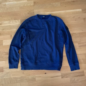 Marinblå sweatshirt från BOSS - Snygg marinblå sweatshirt från BOSS med rund hals och ribbade muddar. Tröjan har ett stilrent BOSS-märke på vänster ärm och är tillverkad i mjuk bomull. Perfekt för dig som gillar enkel och clean stil med premiumkänsla.