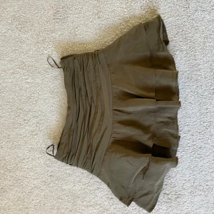 Grön volangkjol från Zara XS - Supersnygg grön kortkjol från Zara med volang och rynkad midja. Kjolen har en flowy och luftig känsla, perfekt för dig som gillar att sticka ut med coola detaljer. Materialet är lätt och skönt, och midjan har en snygg rynkning som ger extra stilpoäng. Kjolen har inbyggda shorts 