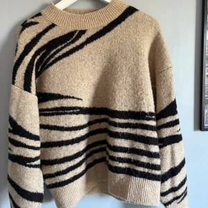 Beige stickad tröja med zebramönster - Säljer en beige stickad tröja med svarta zebraränder. Tröjan har en loose passform, rund hals och långa ärmar med ribbade muddar. 