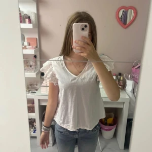 Vit blus med spetsärmar från Only - Supersöt vit blus från Only med v-ringning och korta volangärmar i broderad spets. Luftig och lätt.