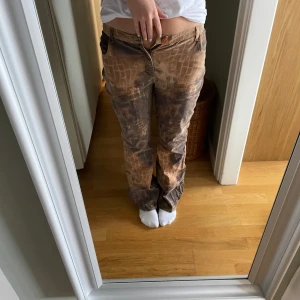 Bruna bootcut byxor med mönster - Unika bruna byxor med coolt  mönster och blekta detaljer. Rakt snitt och klassisk femficksmodell. Byxorna är mid waist . Perfekta för dig som vill sticka ut med en edgy stil.