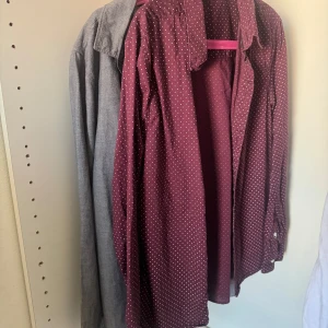 Vinröd prickig och grå skjorta från H&M - Snygg vinröd skjorta från H&M med vita små prickar. Klassisk krage och knappar framtill, långärmad och i mjuk bomull. Perfekt för dig som gillar lite färg och mönster i garderoben. Passar dig som vill ha en chill och stilren look. 30kr för båda. 20kr för en. 