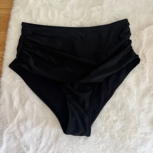 Svart bikiniunderdel high waist - Snygg svart bikiniunderdel med high waist och stilren design. Materialet är mjukt och stretchigt med 82% polyester och 18% spandex, vilket gör dem bekväma och följsamma. Perfekt för strandhäng eller poolparty i sommar!
