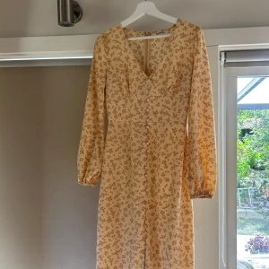 blommig långklänning - Superfin beige långklänning från NA-KD med små blommor i brunt. OBS! Endast ljuset och skuggan som gör högra armen mörkare, inget smuts eller liknande. Använd 2 gånger