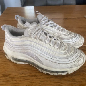 Nike Air Max 97 vita sneakers EUR 38 - Nike Air Max 97 sneakers i helvitt med ikoniska vågiga linjer och synlig Air-sula. Skorna har snörning och en platt sula, tillverkade i syntet och mesh för en sportig vibe. Perfekt för dig som gillar klassisk streetstyle och vill sticka ut med en clean look.