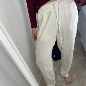 Vita linnebyxor med snörning - Säljer ett par vita linnebyxor med avslappnad passform och elastisk midja med snörning. Byxorna har raka ben och en liten slits vid benslutet. Perfekta för varma dagar och riktigt sköna att bära.