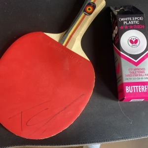 Signerat Truls rack med 3 stycken pingis bollar - Pingisracket från Stiga, 65-årsjubileum, med röd beläggning och signatur på bladet. Paketet inkluderar Butterfly R40+ trestjärniga plastbollar. Perfekt för dig som vill ta ditt bordtennisspel till nästa nivå!