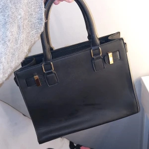 Svart handväska - Snygg svart handväska i skinnimitation med stilrena guldfärgade detaljer och dubbla handtag. Väskan har flera fack med dragkedja och en klassisk, fyrkantig form som rymmer allt du behöver till vardagen. Perfekt för dig som gillar en clean och elegant look.