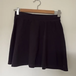 Svart kortkjol från Kappahl - Enkel och stilren svart kortkjol från Kappahl. Kjolen har en lätt utställd form och resår i midjan för skön passform. Perfekt att matcha med en cool t-shirt eller hoodie för en avslappnad look.