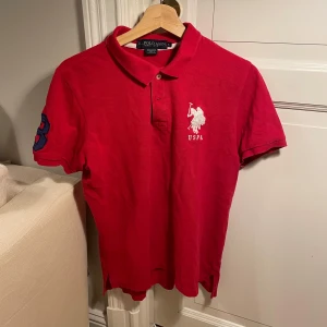 Röd Ralph Lauren piké - Säljer en röd pikétröja från Ralph lauren med klassisk krage, broderad logga på bröstet och stor siffra 3 på ärmen. Tillverkad i 100% bomull, kortärmad och med knappslå framtill. 