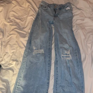 Ljusblå jeans med slitningar från 157 - Säljer ett par ljusblå jeans från 157 i storlek 160. Jeansen har raka ben, slitna detaljer på båda knäna och klassisk femficksdesign. Resår i midjan för extra komfort. Perfekta för en avslappnad och trendig look.