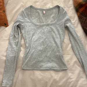 Ljusgrå ribbad topp från Nelly -  ljusgrå långärmad topp från Nelly med ribbad struktur och rundad fyrkantig urringning. 