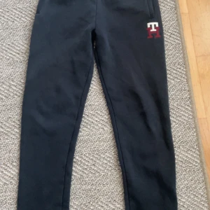 Svarta mjukisbyxor Tommy Hilfiger - Svarta mjukisbyxor från Tommy Hilfiger med broderad TH-logga i vitt och rött på framsidan. Byxorna har en slim passform, ribbad midja och bakficka. Perfekta för chill eller träning, tillverkade i mjukt bomullsmaterial.