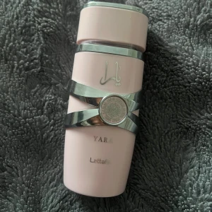 Lattafa Yara parfym rosa flaska - Lattafa Yara parfym i en snygg ljusrosa flaska med silvriga detaljer och arabiska tecken. Flaskan har en unik form med metallband runt och ett matchande lock. Perfekt för dig som gillar stilrena och moderna doftflaskor. Säljer då jag tyvärr inte använder den💕
