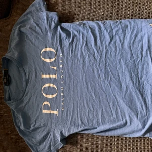 Blå Polo Ralph Lauren t-shirt - Totalt 2-4 små ” sprickor ” i texten men annars som ny,  öppen för prisförslag eller byten, 