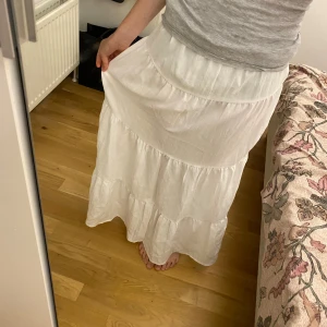 Vit långkjol från H&M Divided XS - Superfin vit långkjol från H&M Divided i storlek XS. Kjolen har flera volanger och är gjord i ett lätt och luftigt material med 74% viskos och 26% polyamid. Perfekt för en chill och somrig look. Säljer den för att den var för lång. Annars är den jättefin och skriv gärna till mig om ni undrar hur lång jag är.