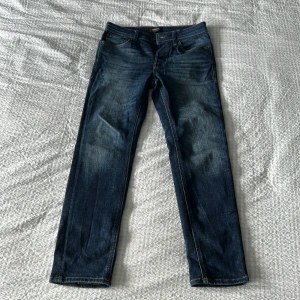 Jack & Jones Tapered Mike jeans blå - Snygga blå jeans från Jack & Jones, modell Tapered Mike. Jeansen har klassisk femficksdesign, normal midja och avsmalnande ben. Tillverkade i slitstarkt denim med snygga slitningar och kontrastsömmar. Perfekta för en avslappnad och trendig look.