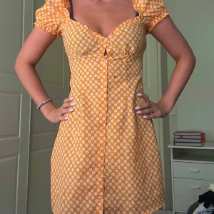 Gul blommig kortklänning med puffärm - Superfin gul kortklänning med vita små blommor och puffärmar. Klänningen har söt v-ringning, knappar framtill och figurnära passform.