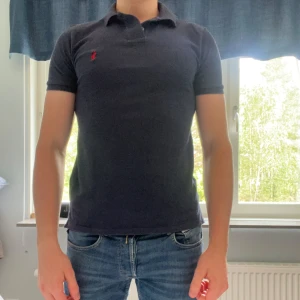 Navy Polo Ralph Lauren pikétröja - Navy pikétröja från Polo Ralph Lauren i custom slim fit. Klassisk krage, korta ärmar och röd broderad logga på bröstet. Tillverkad i mjuk bomull som sitter snyggt och bekvämt. Perfekt för en clean och stilren look. Modellen är 184 cm och väger 81 kg.