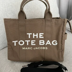 Marc Jacobs Tote bag -  Äkta Marc Jacobs tote bag i grön färg. Använd i ungefär ett år i gott skick med vissa tecken på användning. Extra axelband följer med, justerbart upp till 144 cm. Innerfack finns synliga på bilderna. Lite slitage på fästet av nyckelbandet. Material bomull. Får plats med en 13 tum dator.   Bredd 34 cm Höjd 27 cm Djup 15 cm 