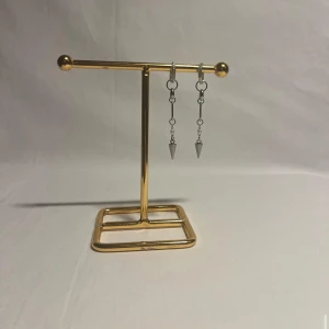 Silvriga kedjeörhängen med spetsig berlock - Säljer ett par coola örhängen i silverfärgad metall med kedjor och spetsiga konformade berlocker. Örhängena har små ringar upptill och hänger snyggt från örat, perfekt för dig som gillar edgy detaljer.