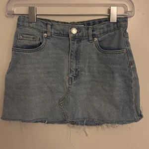 Levi's jeanskjol mini - Snygg ljusblå jeanskjol från Levi's med klassisk femficksdesign och rå, fransig nederkant. Kjolen har bälteshällor och knappstängning framtill. Perfekt för dig som gillar en avslappnad och trendig stil.