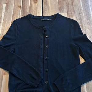 Svart kofta från 157, XS - En klassisk svart kofta från 157 i storlek XS. Koftan har rund halsringning, långa ärmar och knäppning med svarta knappar framtill. Perfekt att slänga över en t-shirt eller linne för en clean och enkel look.💕